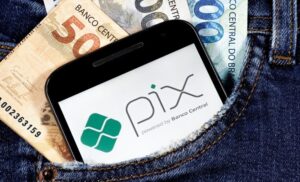 Notas de dinheiro e celular com a logo do Pix aberto